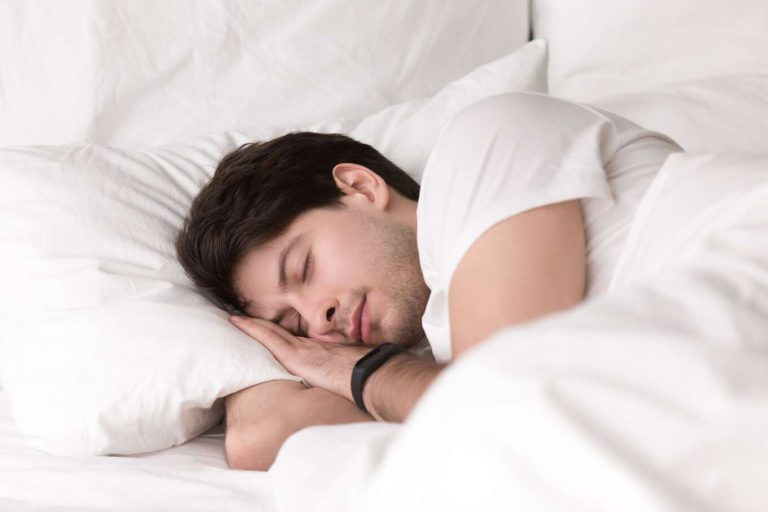 young guy sleeping bed wearing smartwatch sleep tracker